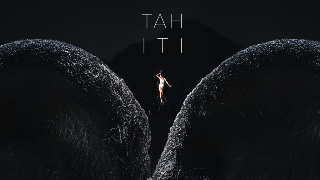 Aerial photograph of a person between waves on black sand at Lafayette Beach in Tahiti